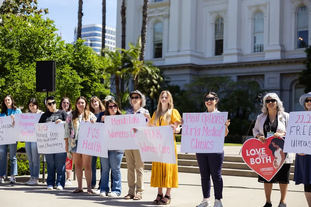 Women hold signs naming California pregnancy centers outside the State Capitol at the California March for Life.
