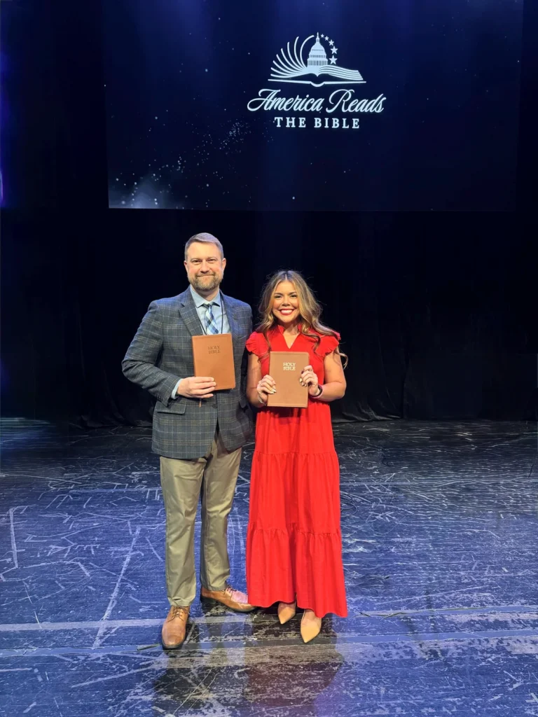 Jonathan Keller and Sophia Lorey hold Bibles on stage at America Reads the Bible in 2026.