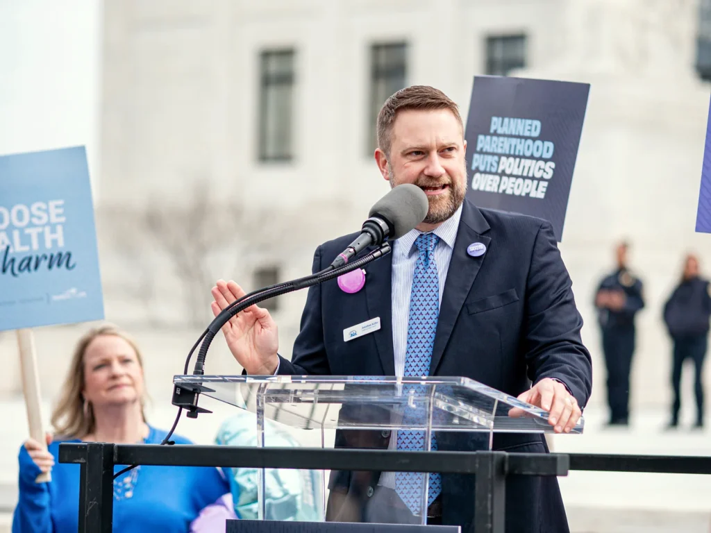 Jonathan Keller speaks from a podium at a rally outside the U.S. Supreme Court in 2025.